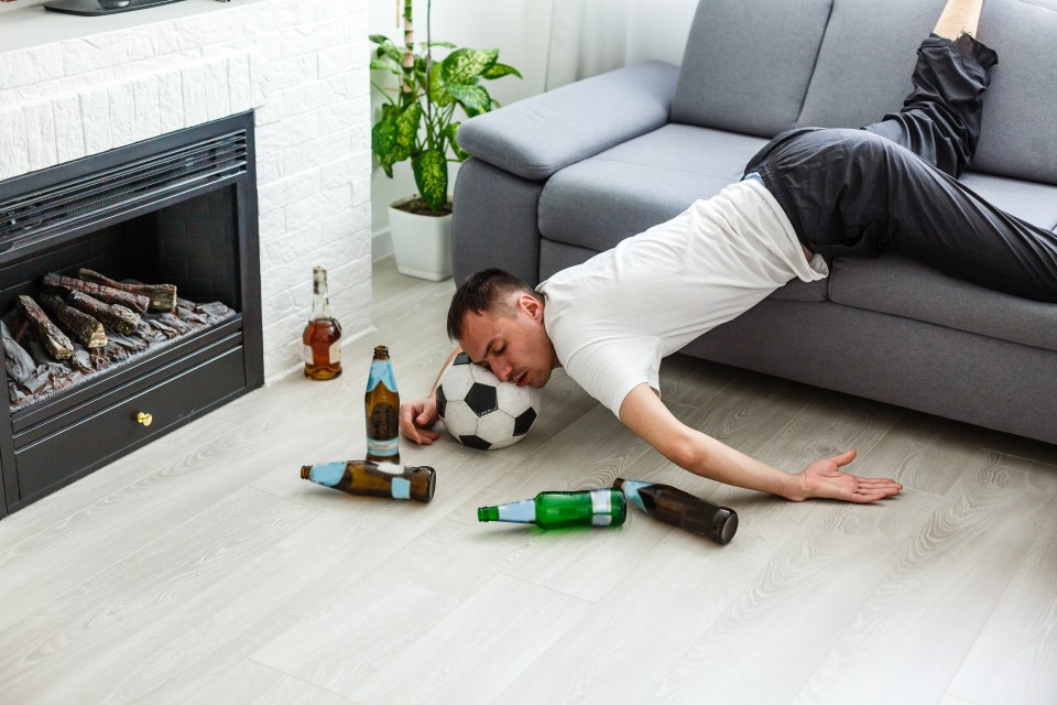 Drunk Young Handsome Man Resting on Couch in the Living Room with Head on the Floor.