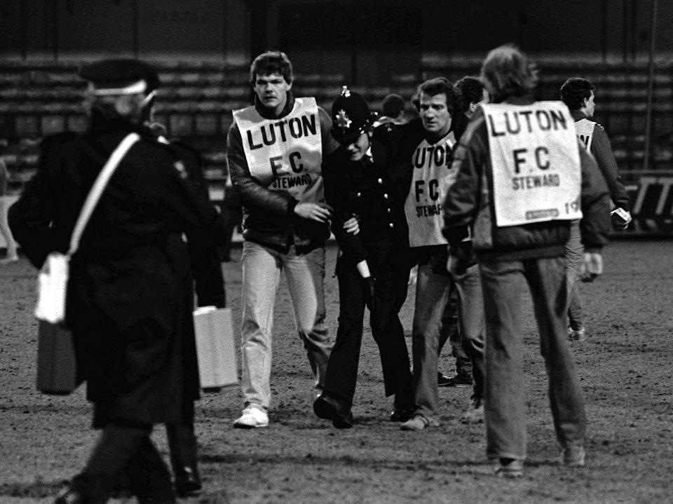Luton FC stewards assisting an injured policeman on the field.