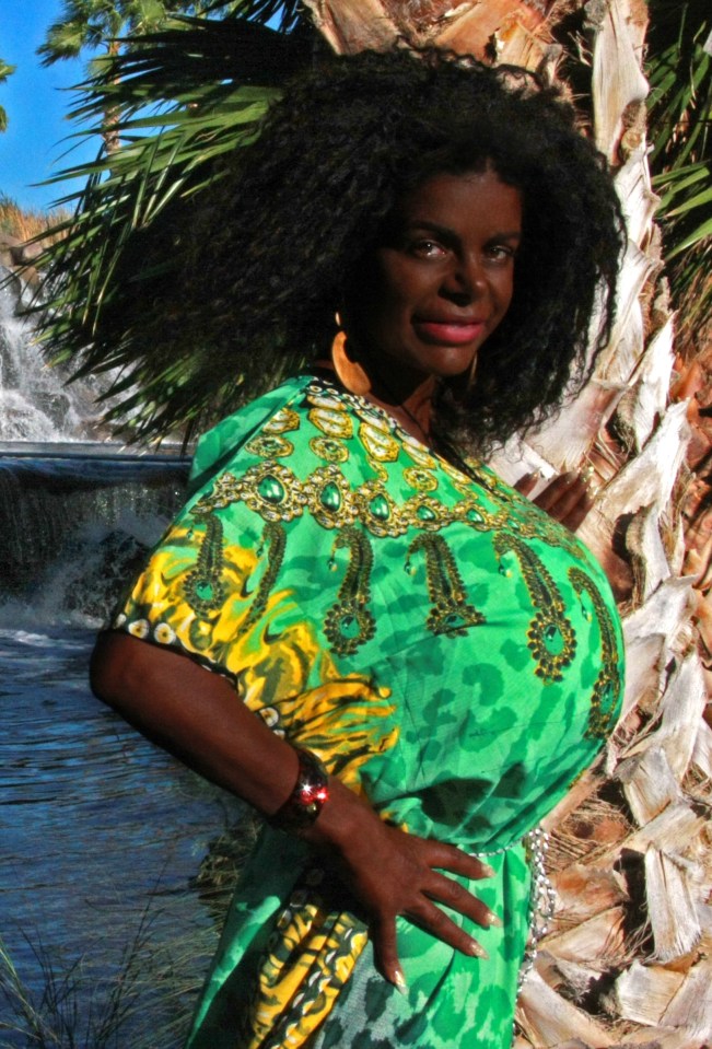 Martina Big, a tanning addict who identifies as a Black woman, posing near a waterfall.