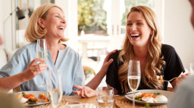 Two women laughing together at a table with drinks and food.