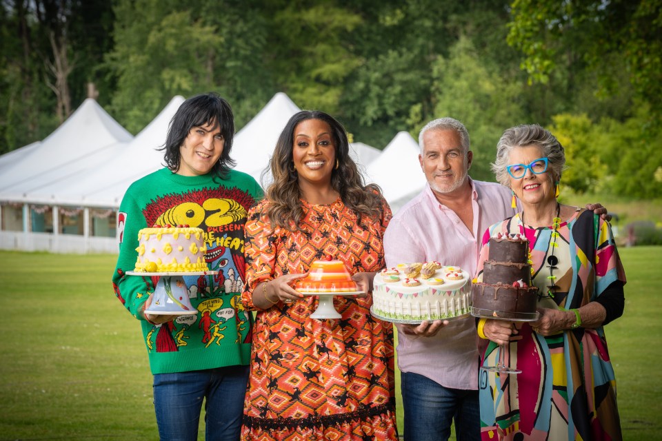 The Great British Bake Off judges and hosts Noel Fielding, Alison Hammond, Paul Hollywood, and Prue Leith posing with cakes and a dessert.