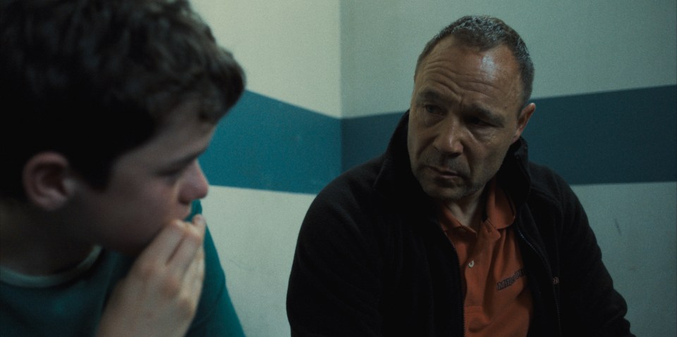 Still from *Adolescence*, showing Owen Cooper as Jamie Miller and Stephen Graham as Eddie Miller in a conversation.
