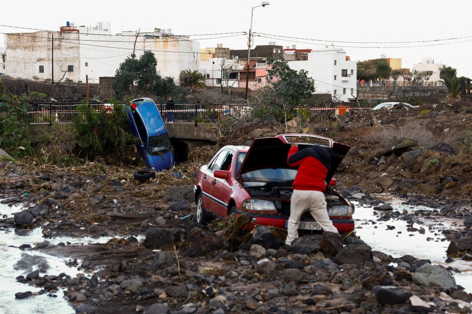 A person inspects a damaged car after a flood.