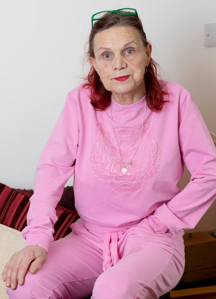 A woman in a pink tracksuit sits and looks at the camera.