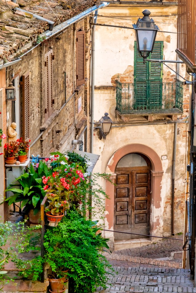 Narrow alleyway in Penne, Italy, with potted plants and old buildings.
