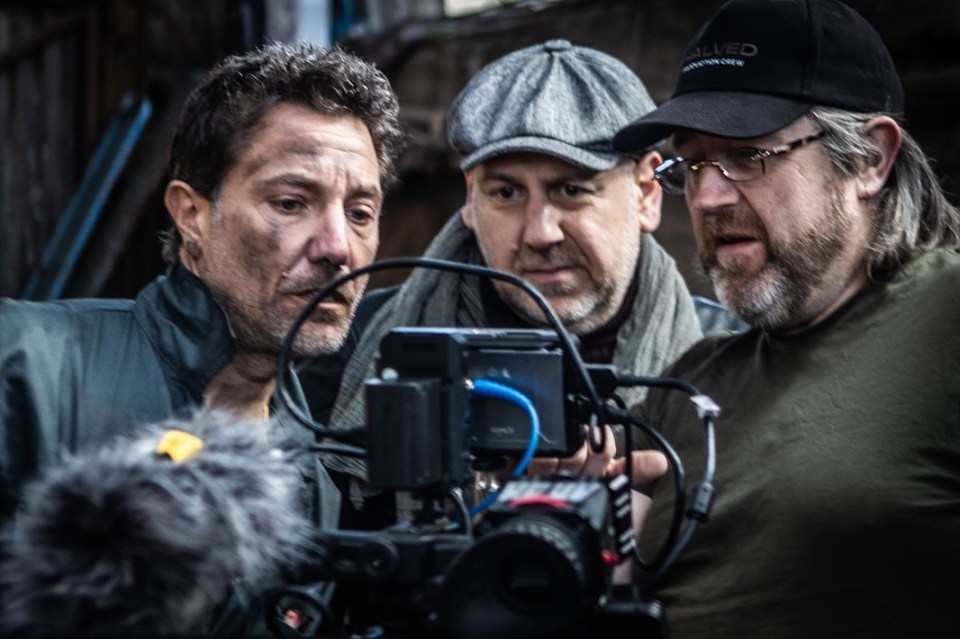 Three men looking at a film camera.