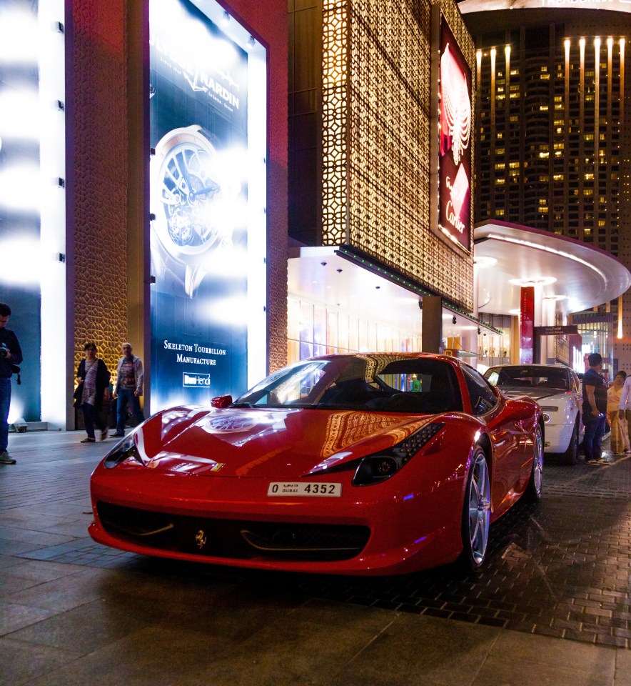 Red Ferrari parked outside Dubai Mall at night.