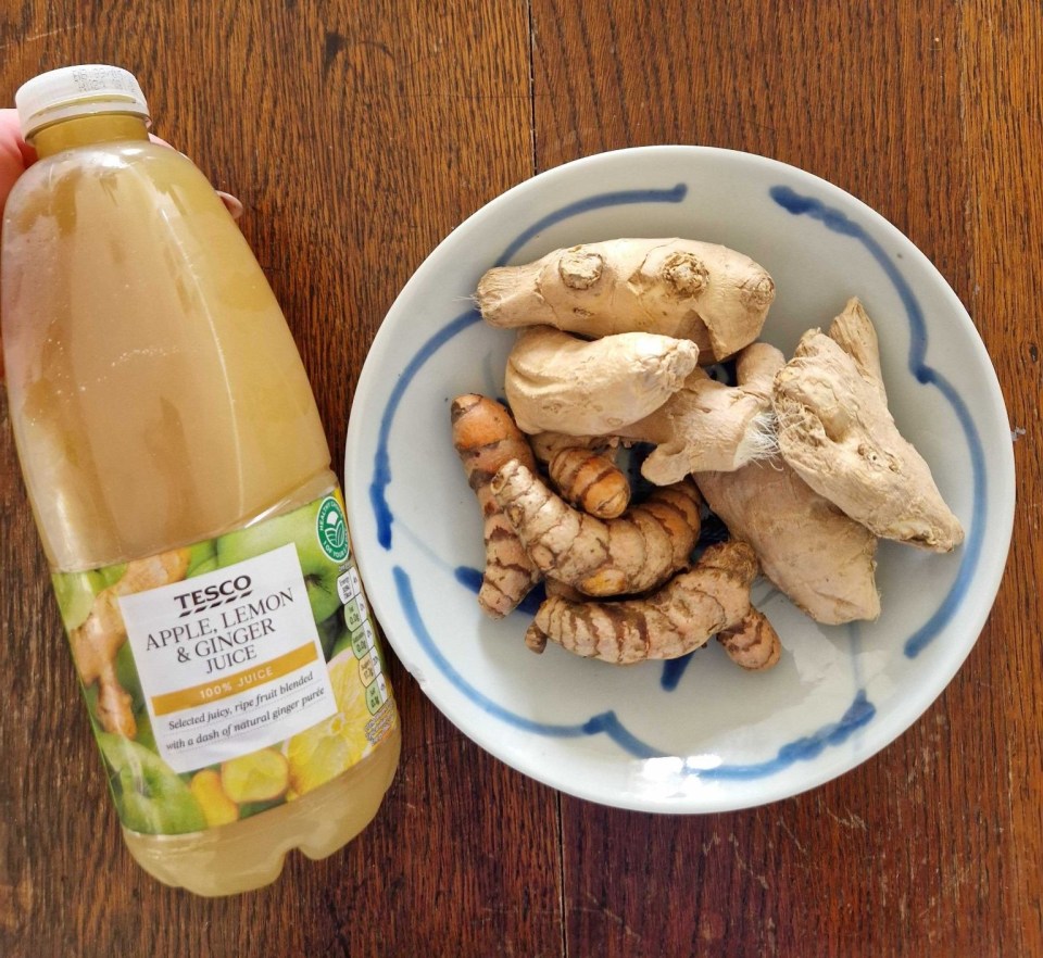 Bottle of apple, lemon, and ginger juice next to ginger and turmeric roots.