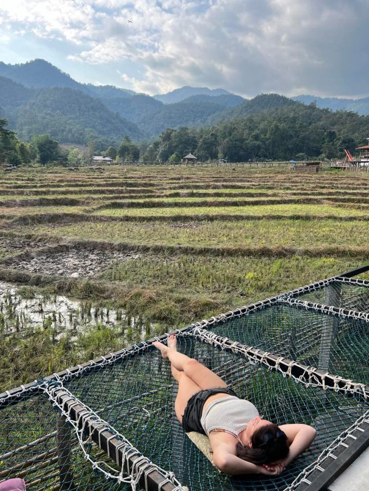 Woman relaxing on a net bed overlooking a rice paddy and mountains.
