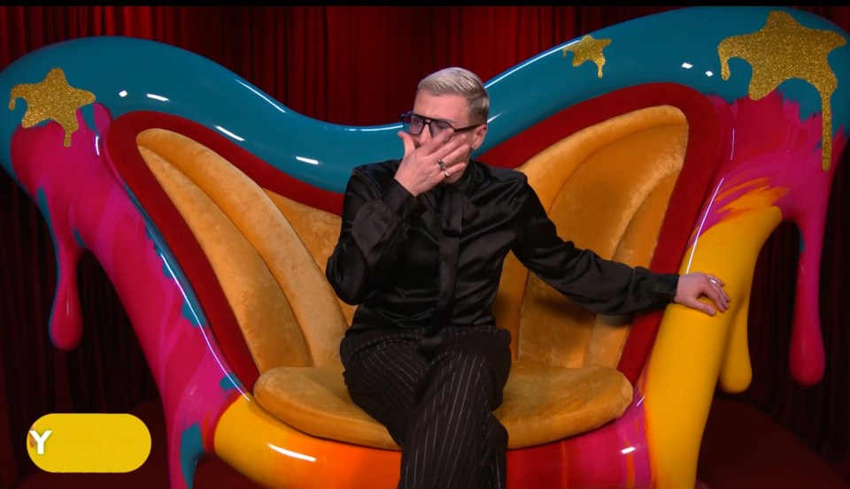 Person sitting in a colorful, abstract chair, covering their face with their hand.