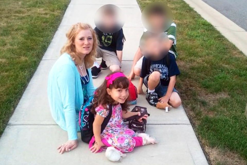 A woman and four children sitting on a sidewalk.