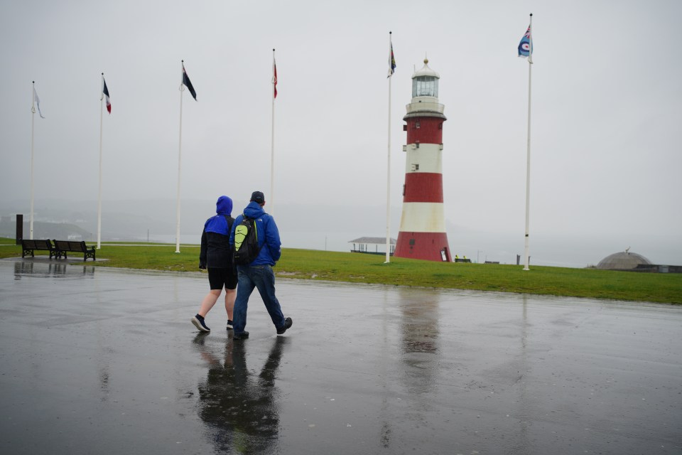 Two people walking in the rain toward a lighthouse.
