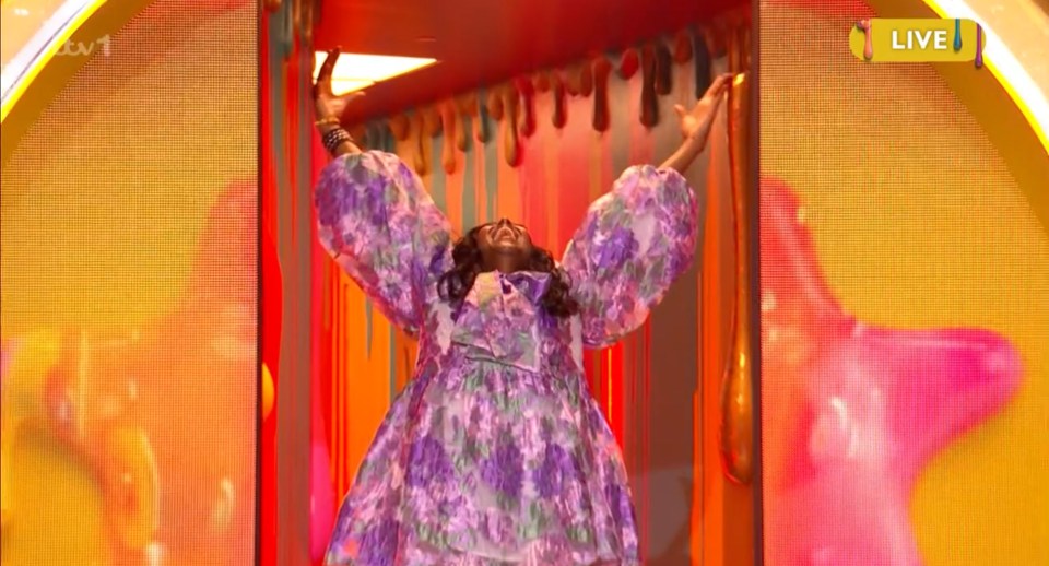 Woman in floral dress with arms raised in a brightly lit doorway.