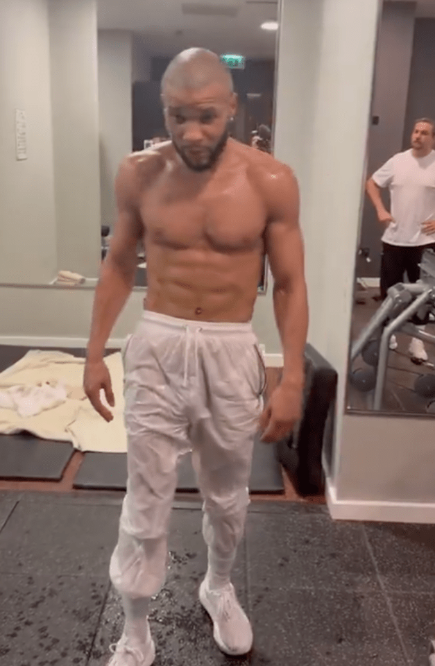 Shirtless man in white sweatpants in a gym.