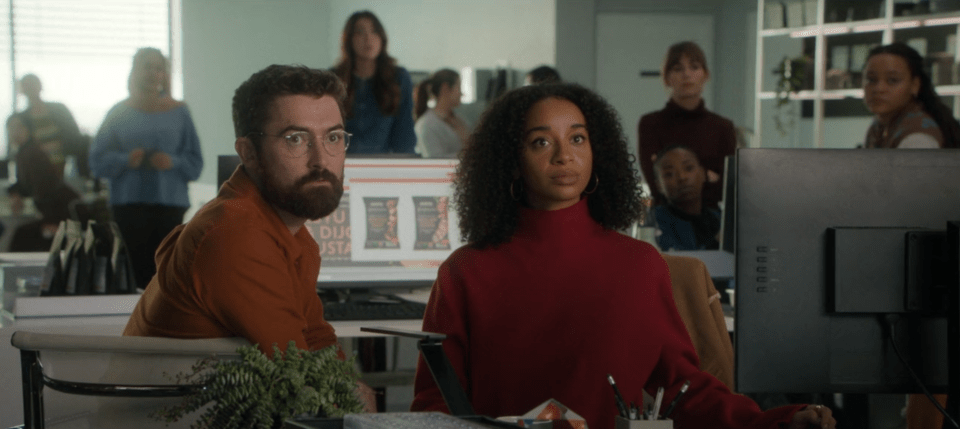 Scene from Black Mirror season 7, episode 2: two colleagues sit at a desk in an office, looking at a computer screen.