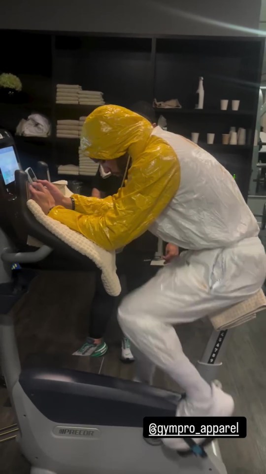 Chris Eubank Jr. on a stationary bike wearing a yellow raincoat and white suit.