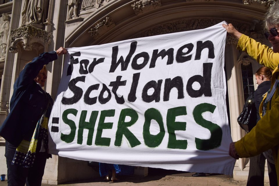 Protestors holding a banner that reads "For Women Scotland =SHEROES" outside a courthouse.