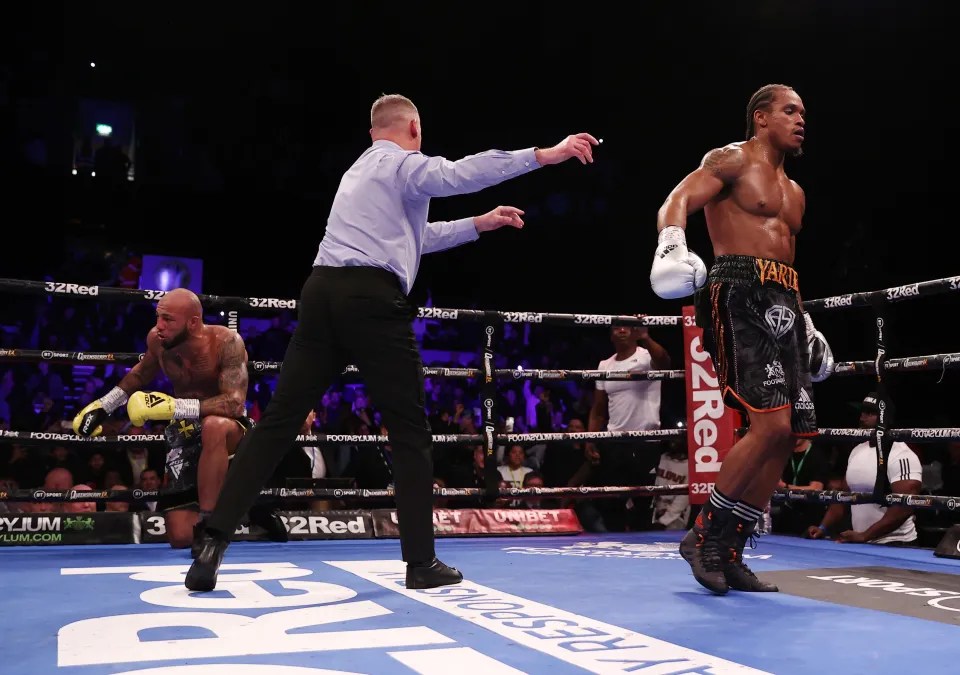 A boxer on one knee in a boxing ring, while a referee signals a knockout.