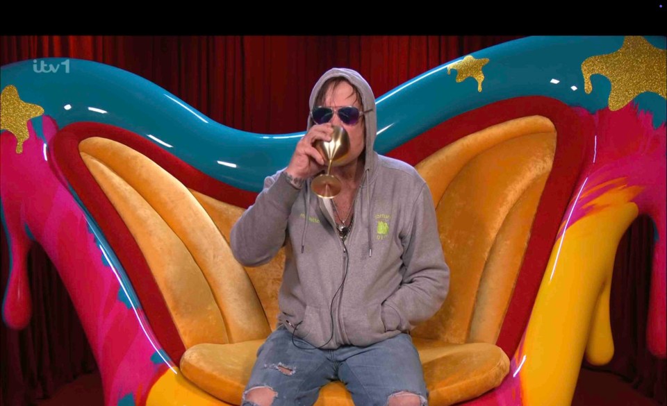 Mickey Rourke drinking from a golden goblet while sitting in a brightly colored chair.