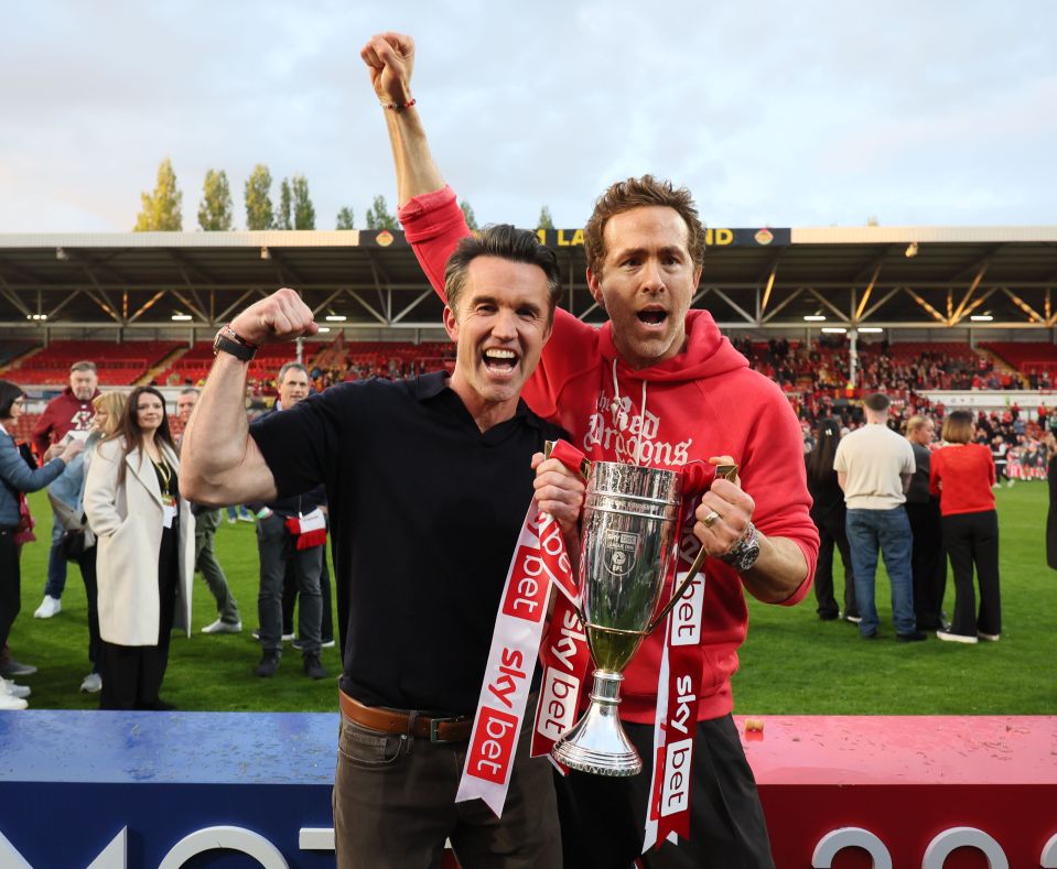 Rob McElhenney and Ryan Reynolds celebrating with a trophy.