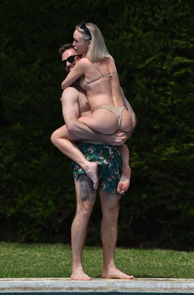 A man carrying a woman in a bikini by the pool.