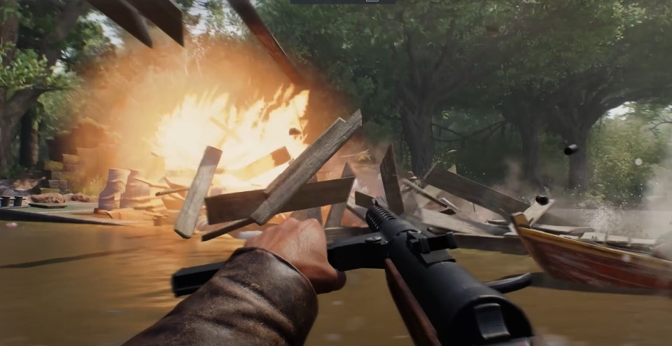 First-person view of a video game, showing a player firing a submachine gun at a wooden structure that explodes in flames.