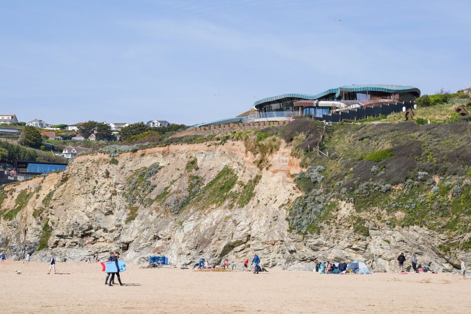 Beach scene with a modern building on a cliff overlooking the sand.