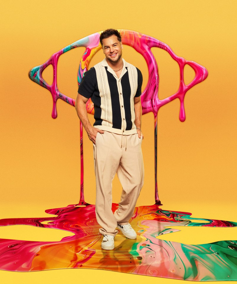 Chris Hughes standing in front of a large, colorful eye graphic for Celebrity Big Brother.