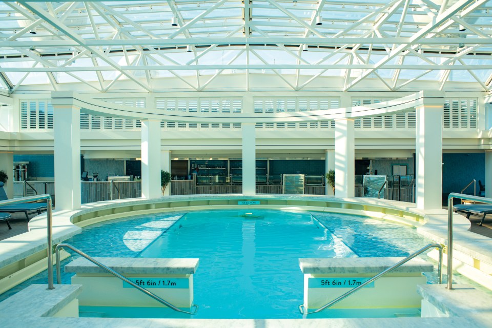 Indoor pool with a glass ceiling and surrounding bar area.