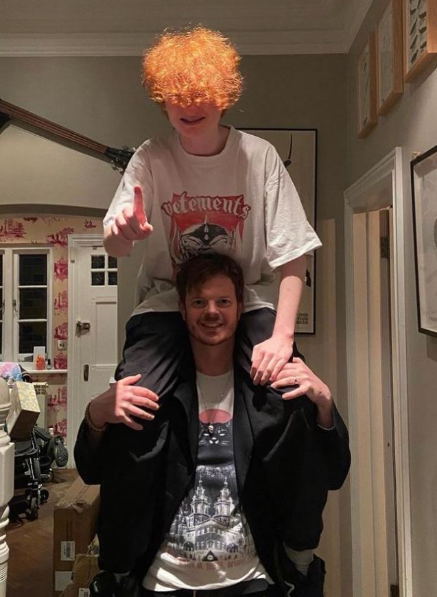 A young man with bright orange hair sits on his father's shoulders.