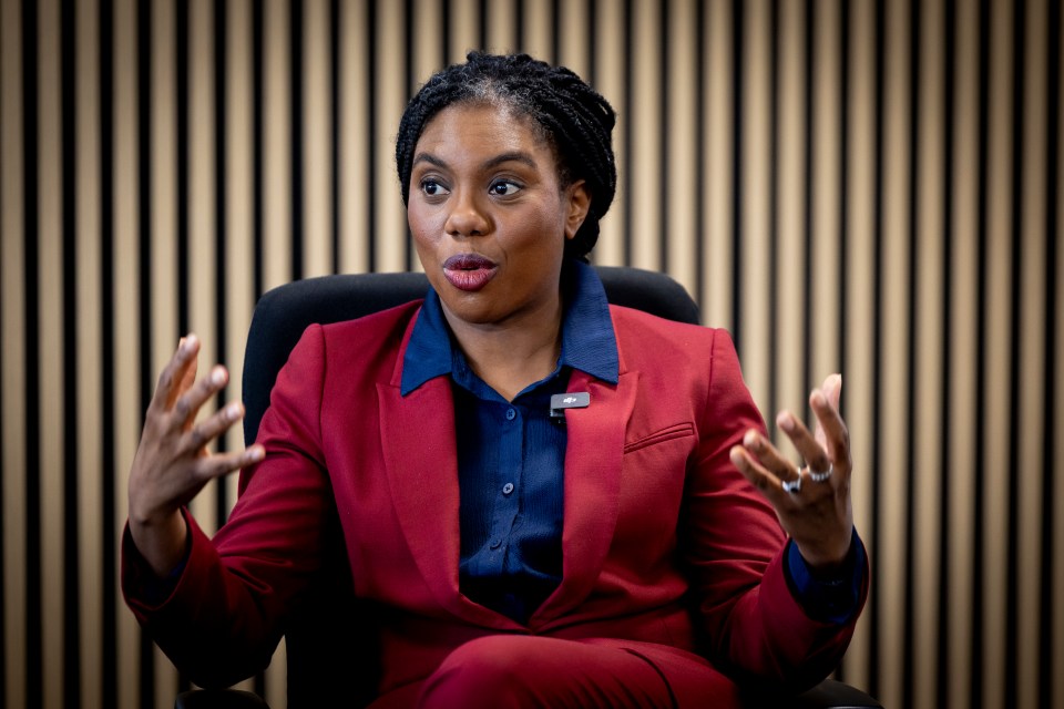 Kemi Badenoch in a red suit jacket, giving an interview.
