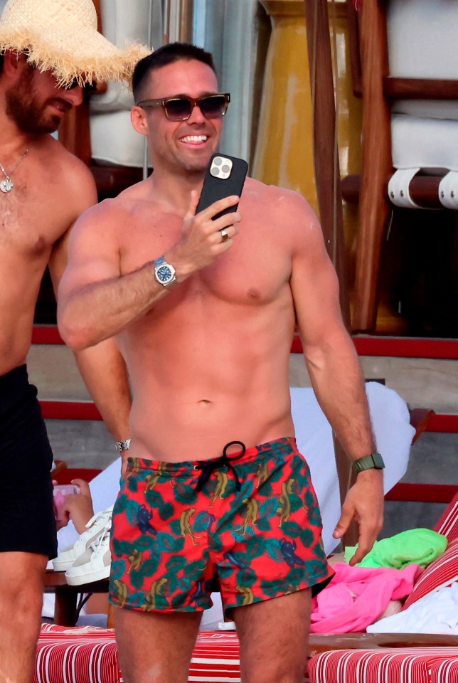 Spencer Matthews shirtless on a beach, holding a phone.