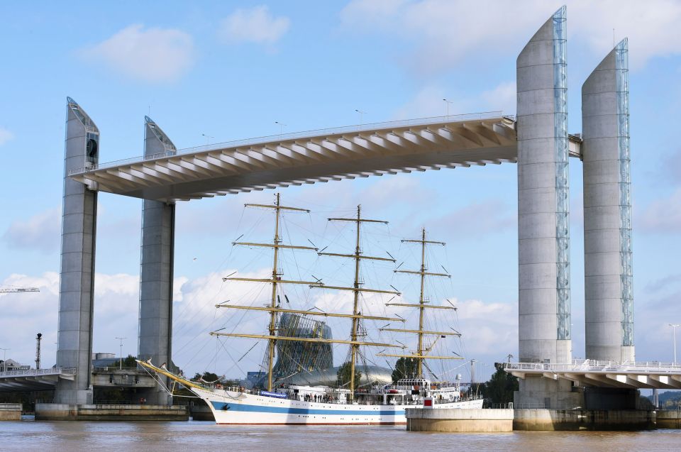 A three-masted sailing ship passing under a modern lift bridge.