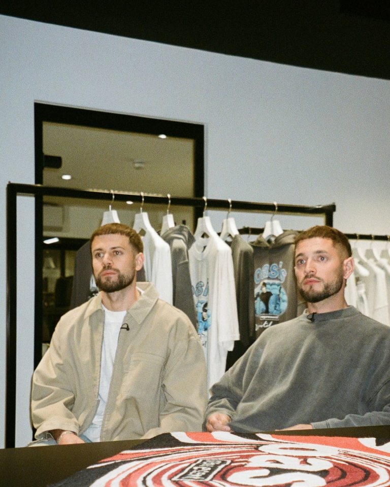 Two men sitting in front of clothing racks.