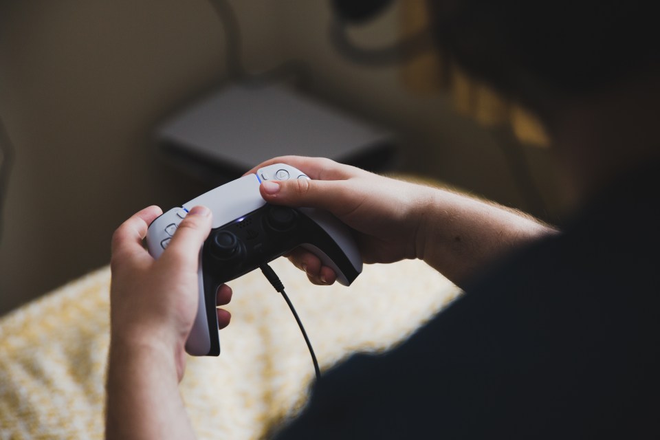 Teenage boy playing video games with a PlayStation 5 controller.