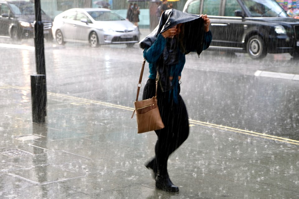 Woman walking down a city street in heavy rain, using a jacket as a makeshift shelter.