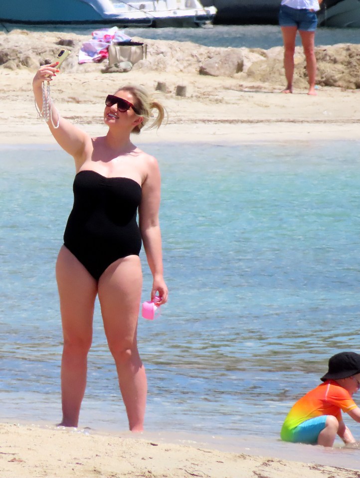 Woman in black swimsuit taking a selfie on a beach.