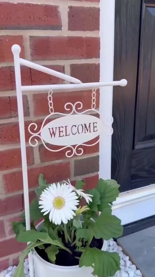 White welcome sign with a potted daisy plant.