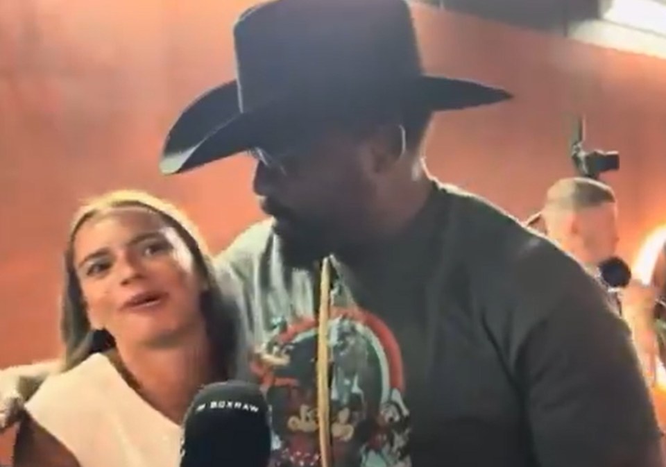 A man in a cowboy hat speaks with a woman in front of a microphone.