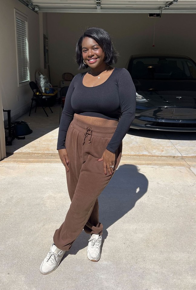 Woman in brown pants and black top standing in front of her garage and Tesla.