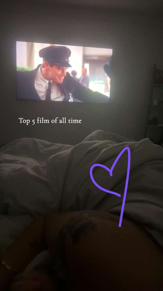 Couple in bed watching a movie projected on the wall; the movie is labeled as a top 5 film of all time.