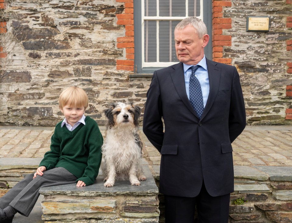 A boy, a dog, and a man in a suit stand outside a stone building.