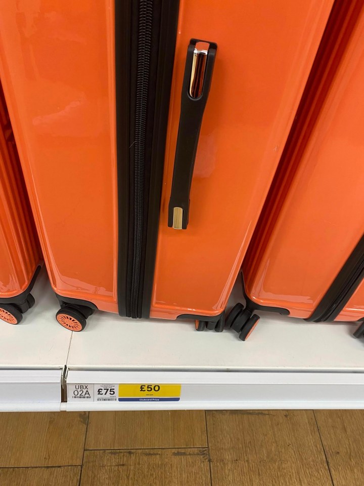 Orange suitcases on a store shelf with price tags.
