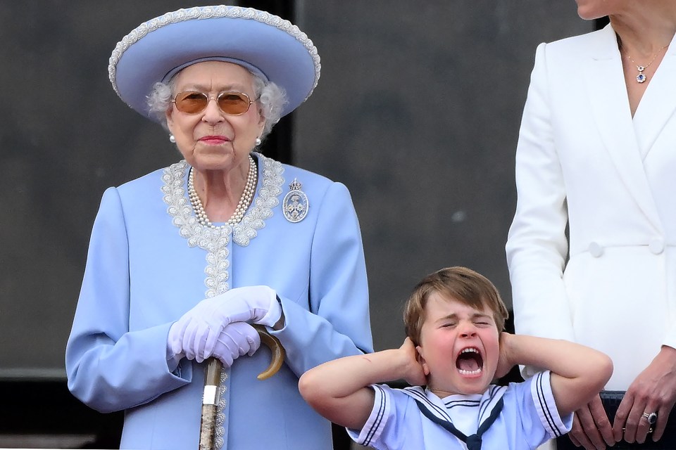 Prince Louis covering his ears next to Queen Elizabeth II on a balcony.