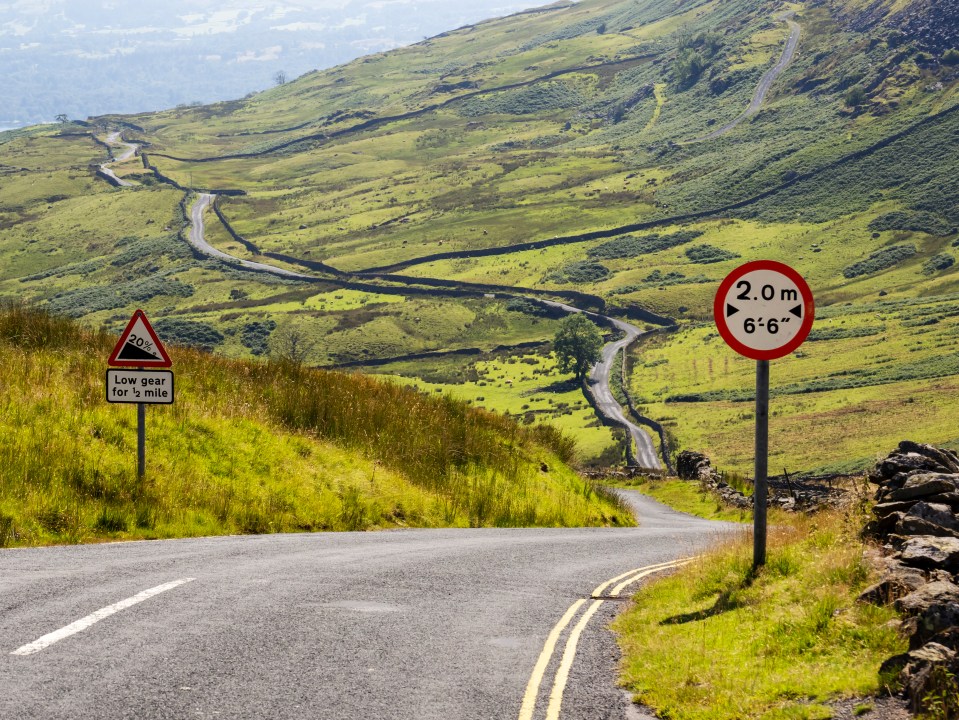 Winding road in the Lake District with road signs indicating steep incline and maximum width.