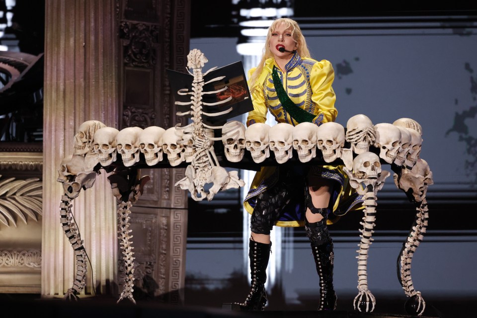 Lady Gaga performing at Copacabana Beach, seated at a piano made of skulls and skeletons.