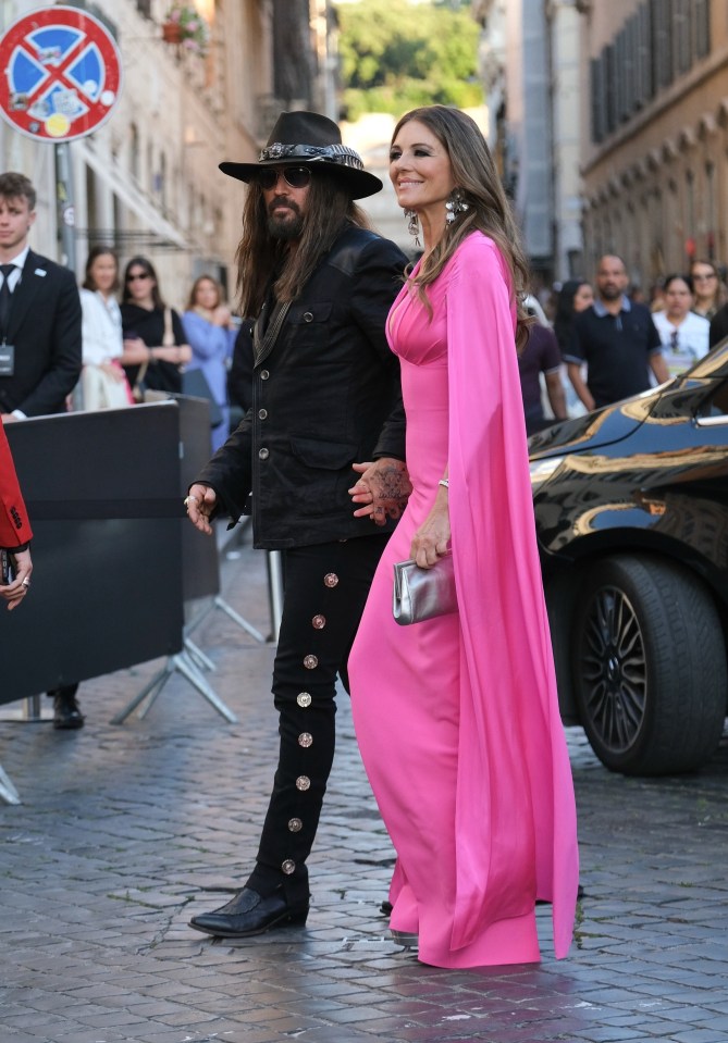 Liz Hurley and Billy Ray Cyrus walking hand-in-hand at a red carpet event.