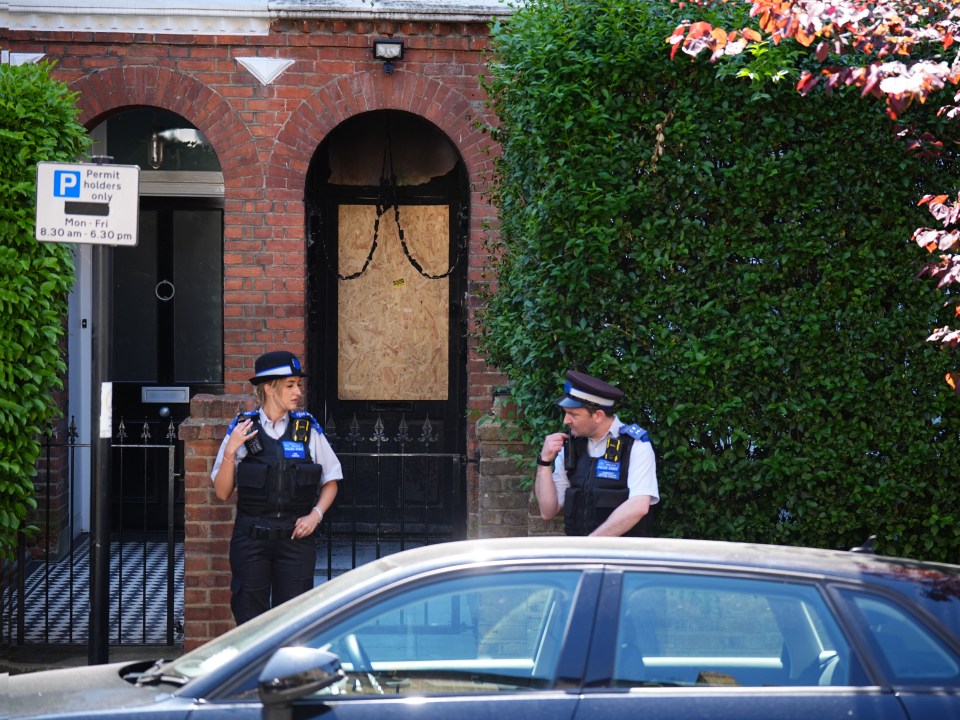 Two police officers standing outside a house with a boarded-up door following a suspected arson attack.