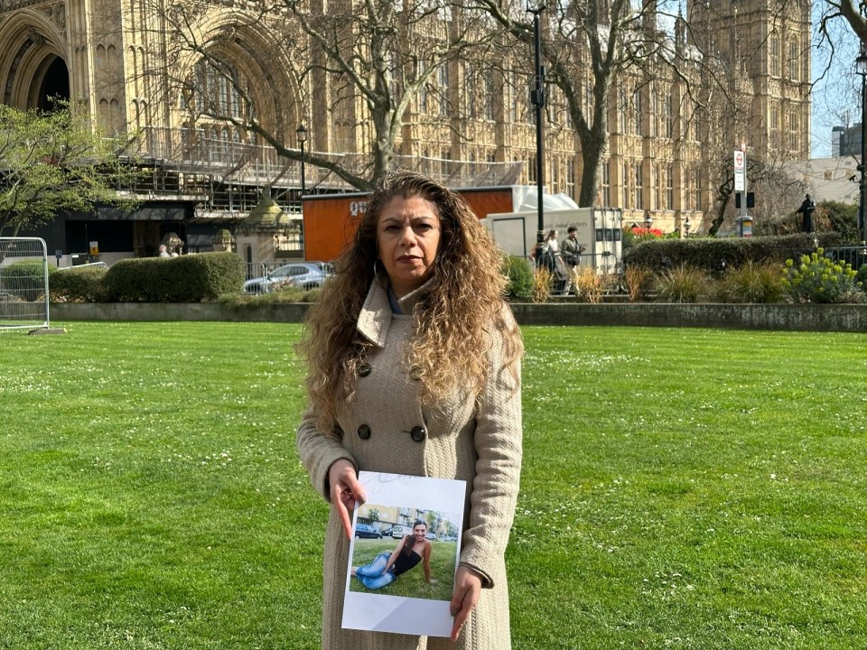 Woman holding a photo of a young woman in front of the Houses of Parliament.