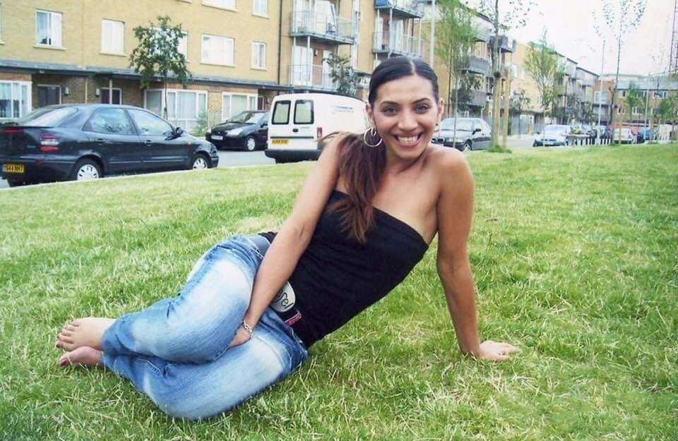 Woman sitting on grass in front of apartment buildings.